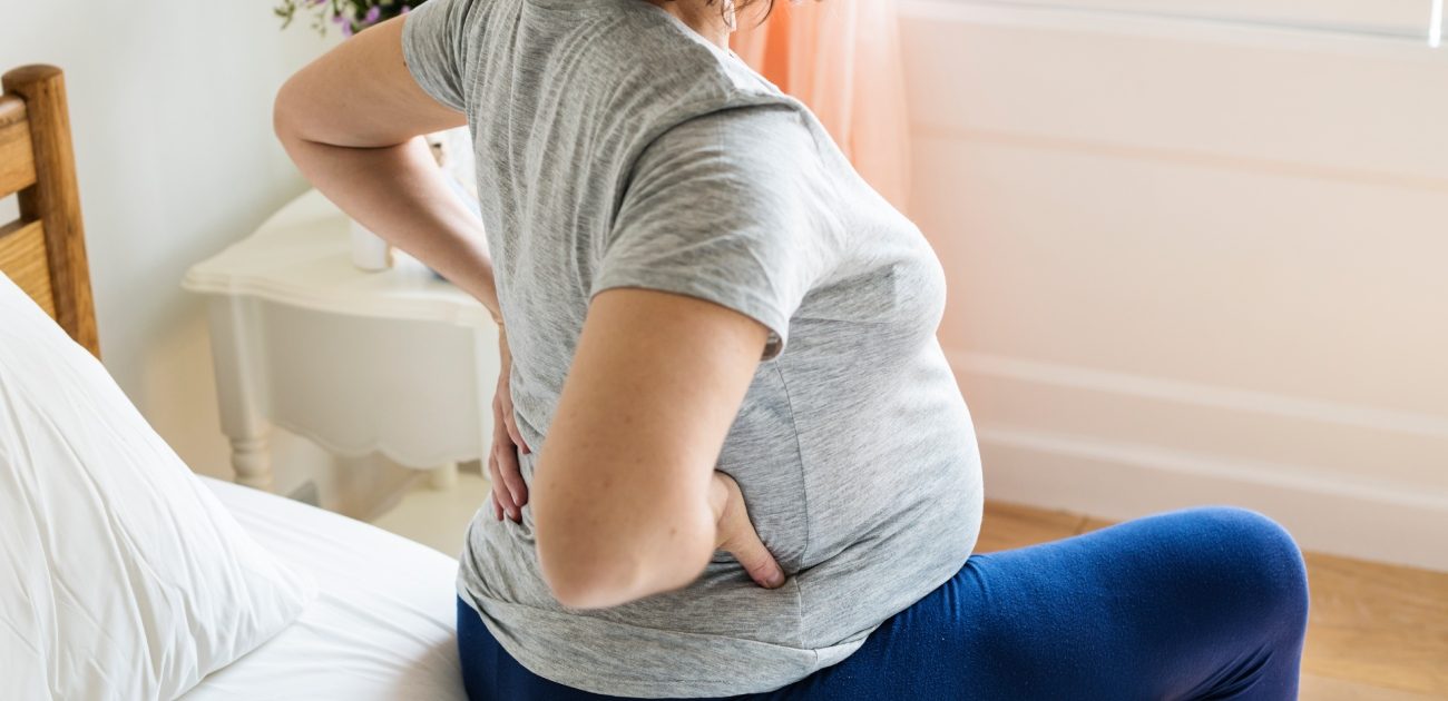 امرأة حامل تجلس على طرف السرير وتُعاني من ألم في الظهر