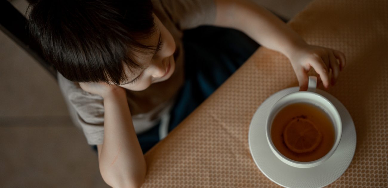 طفل يجلس ويمسك بطرف كوب من الشاي على الطاولة