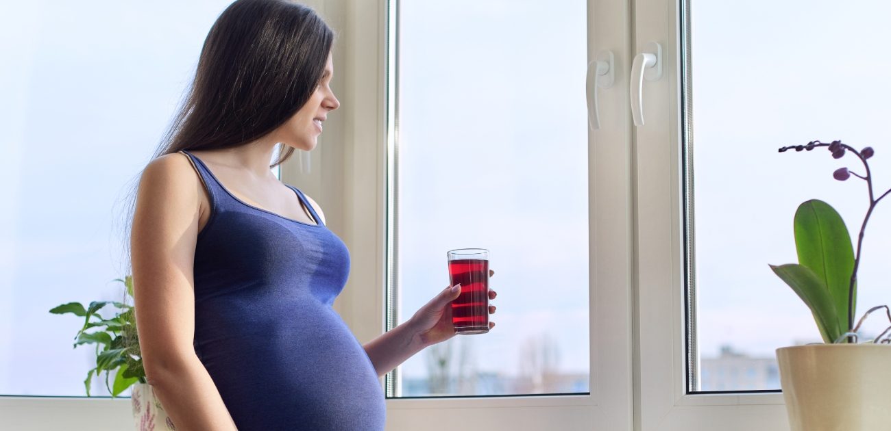 امرأة حامل تُمسك كوب من العصير وتنظر إلى الخارج