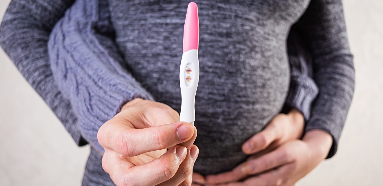 امرأة حامل تمسك اختبار حمل ويُعانقها زوجها من الخلف