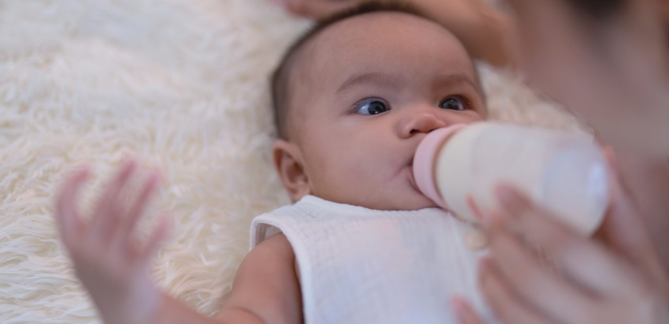 طفل يشرب الحليب بالزجاجة التي تمسك بها والدته وينظر إليها