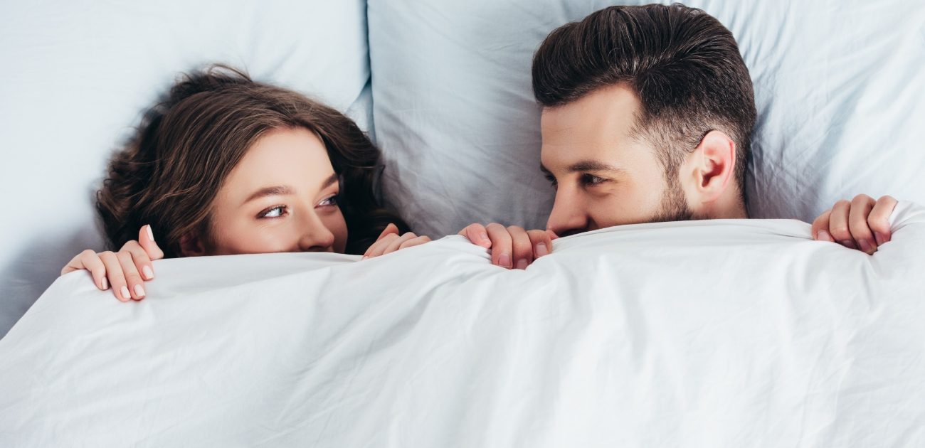 زوجان ينظران إلى بعضما البعض بسعادة من تحت غطاء السرير