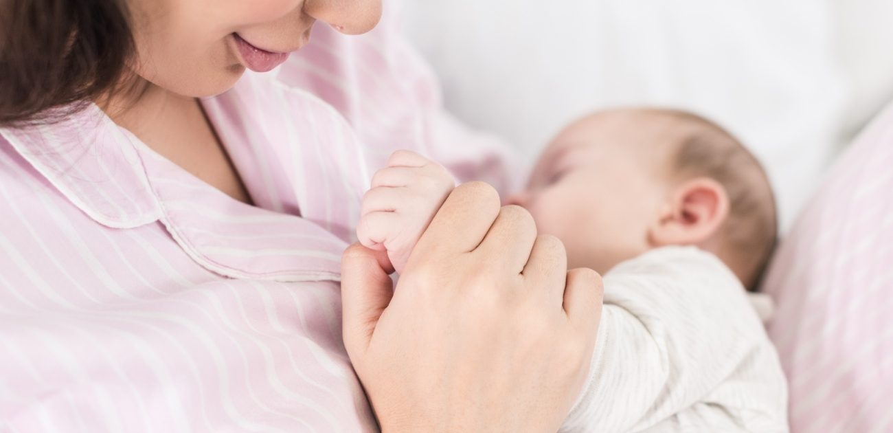 طفل يرضع من والدته وهي تمسك يده ومبتسمة
