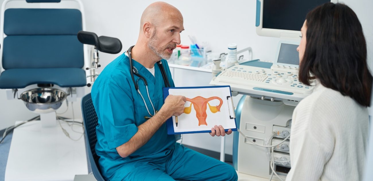 طبيب يشرح لمريضته في عيادته وهو يمسك صورة للجهاز التناسلي الأنثوي