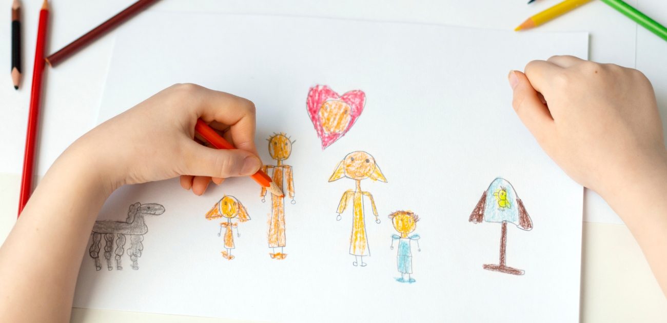 يدي طفل يرسم عائلته بالألوان على ورقة