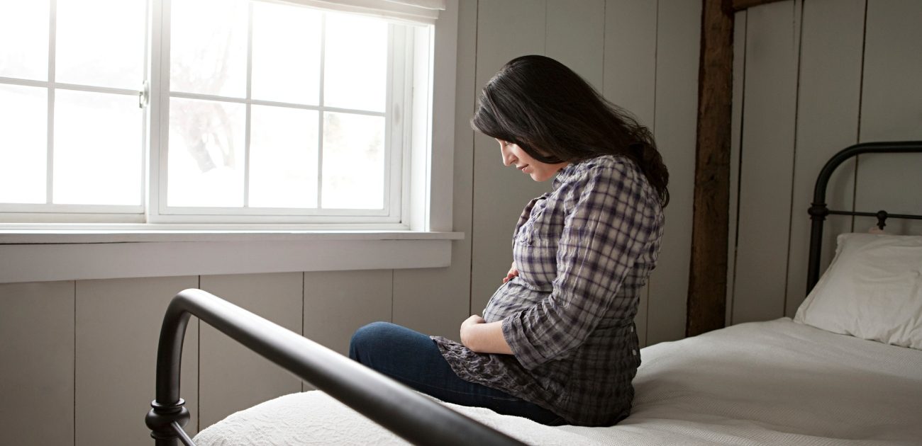 امرأة حامل تجلس على السرير وتضع يديها على بطنها أثناء النظر إليه