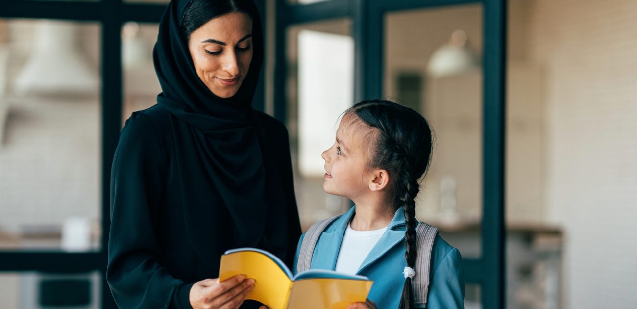 أمّ عربيّة تُمسك الدفتر مع ابنتها التي تستعدّ للذهاب إلى المدرسة