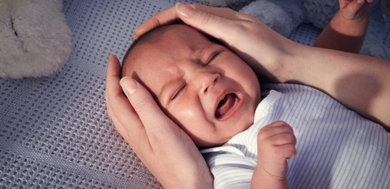طفل رضيع يبكي وأمّة تضع يديها حول رأسه