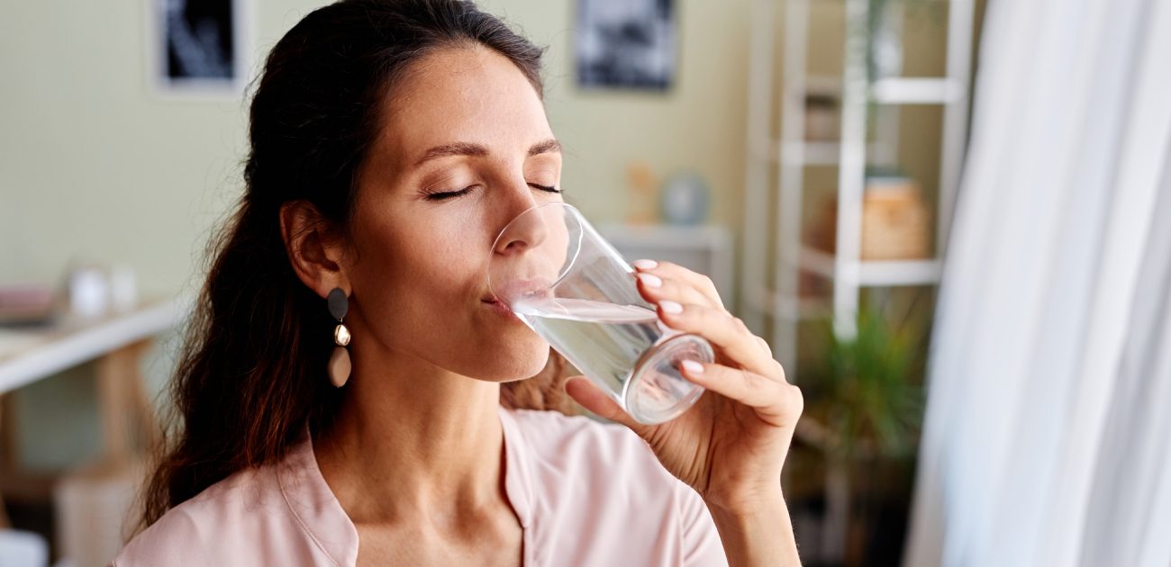 امرأة تشرب كوب من الماء وهي تغمض عينيها