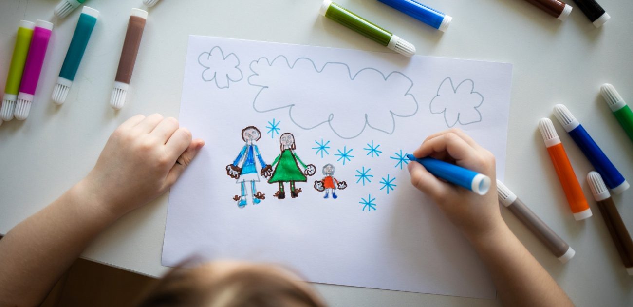 طفل يرسم نفسه مع والديه على ورقة بالألوان