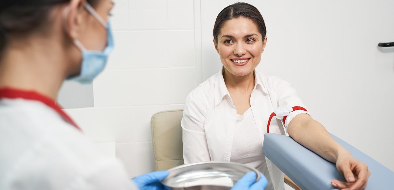 امرأة مبتسمة تنظر إلى الممرّضة أثناء التجهيز لسحب الدم