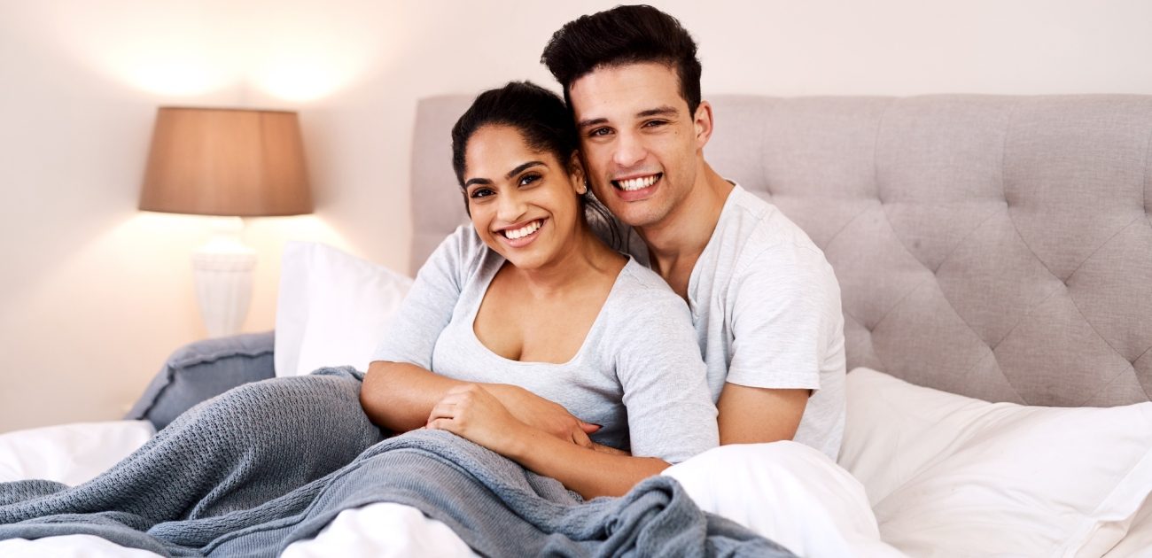 زوج يحضن زوجته على السرير وهما مُبتسمان