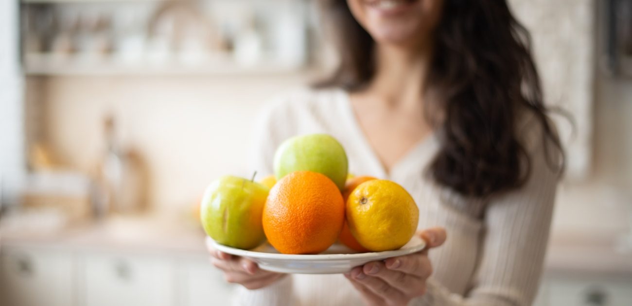 امرأة تُمسك صحن يحتوي ليمون وتفاح وبرتقال