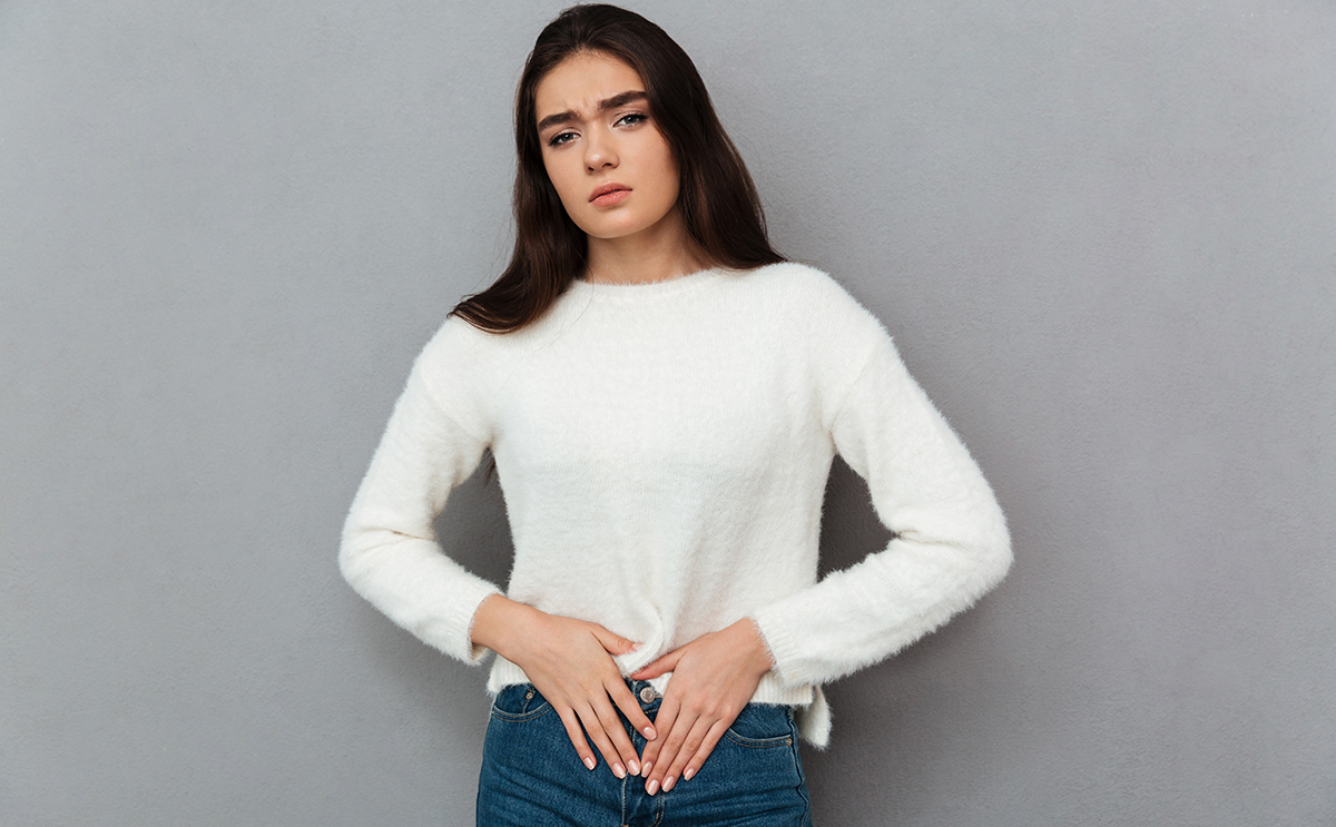 إمرأة متألّمة تضع يديها على بطنها