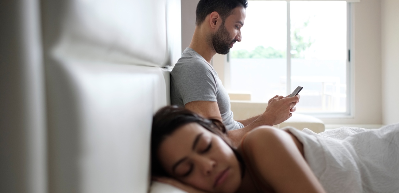 زوج يتحدث بالسر على هاتفه خلال نوم زوجته