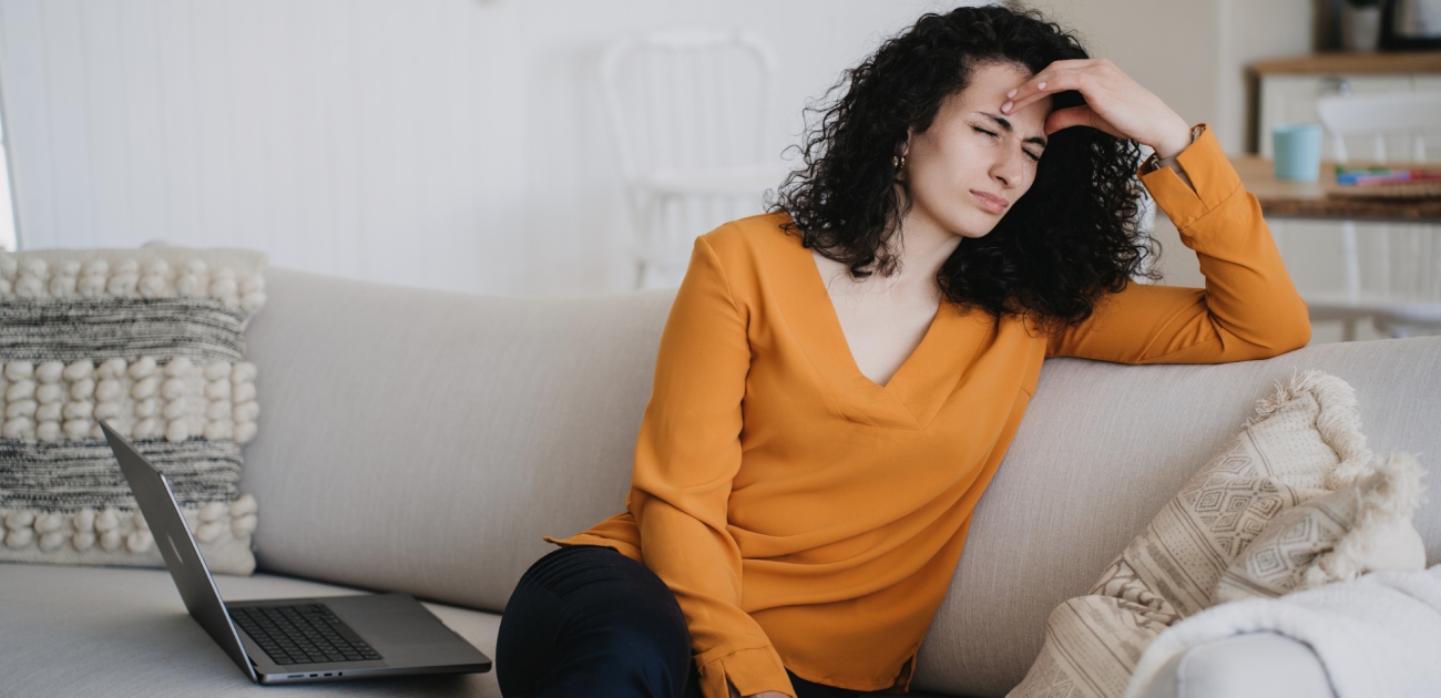 امرأة مُتعبة تجلس على الكنبة وتضع يدها على رأسها