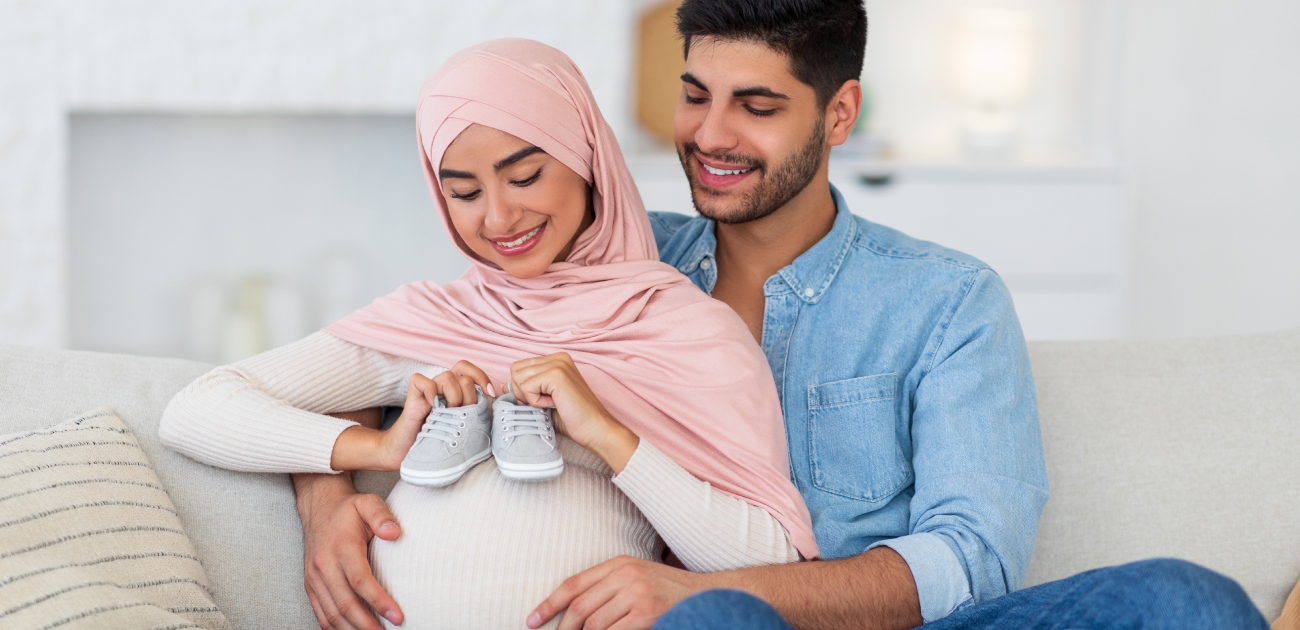 زوج يُعانق زوجته الحامل التي تمسك حذاء مولود جديد بسعادة