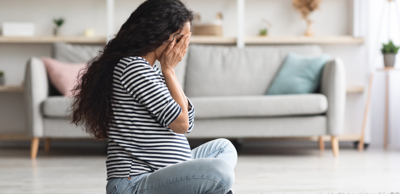 امرأة حامل حزينة تجلس على الأرض وتضع يديها على وجهها