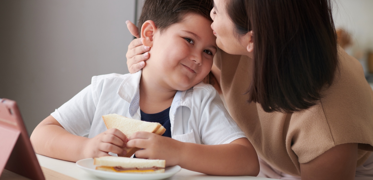 أمّ تقبّل طفلها على رأسه أثناء تناوله الطعام