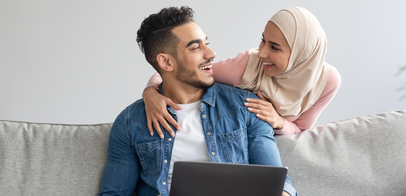 امرأة تحضن زوجها من الخلف وهو يحمل الحاسوب