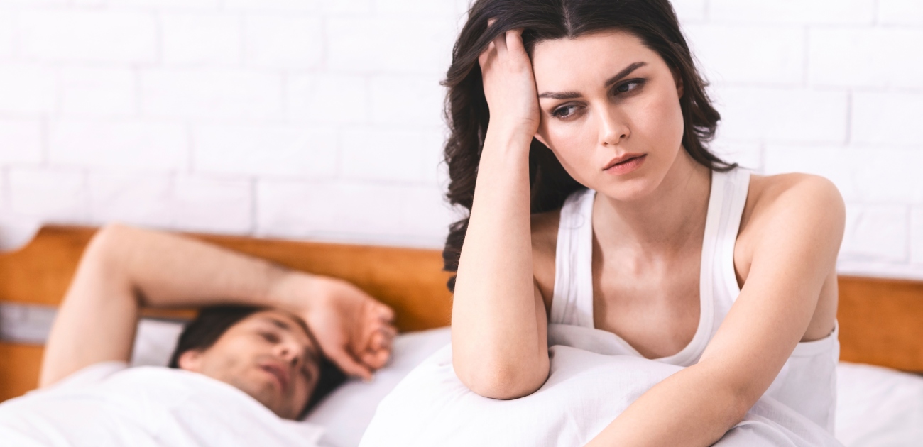 رجل نائم وامرأة تجلس بجانبه على السرير غير سعيدة