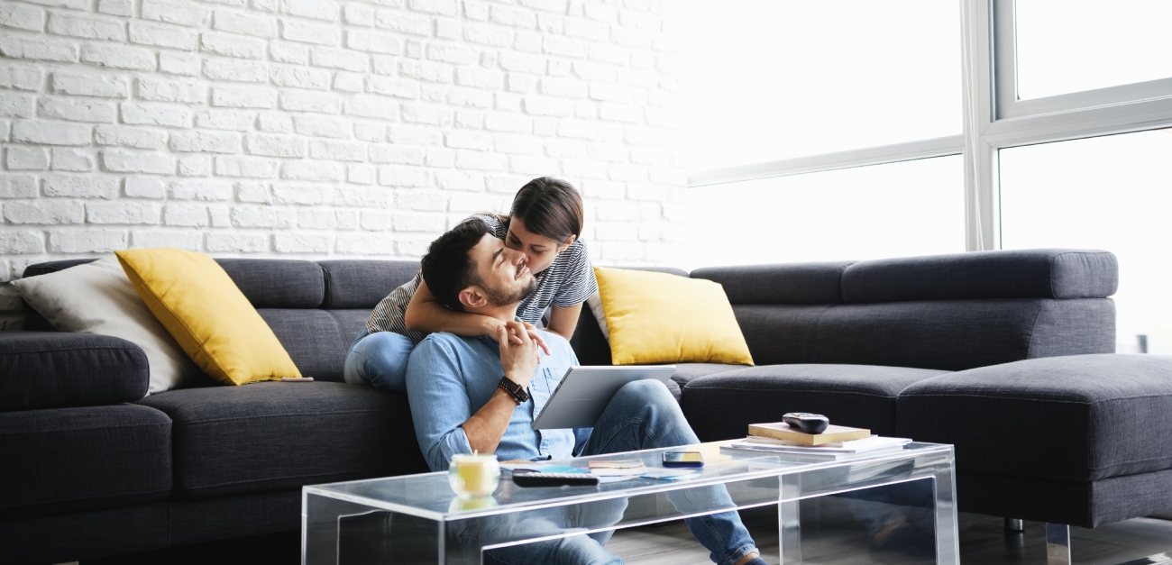 رجل يجلس على الأرض وزوجته تجلس خلفه على الكنبة وتقبّله