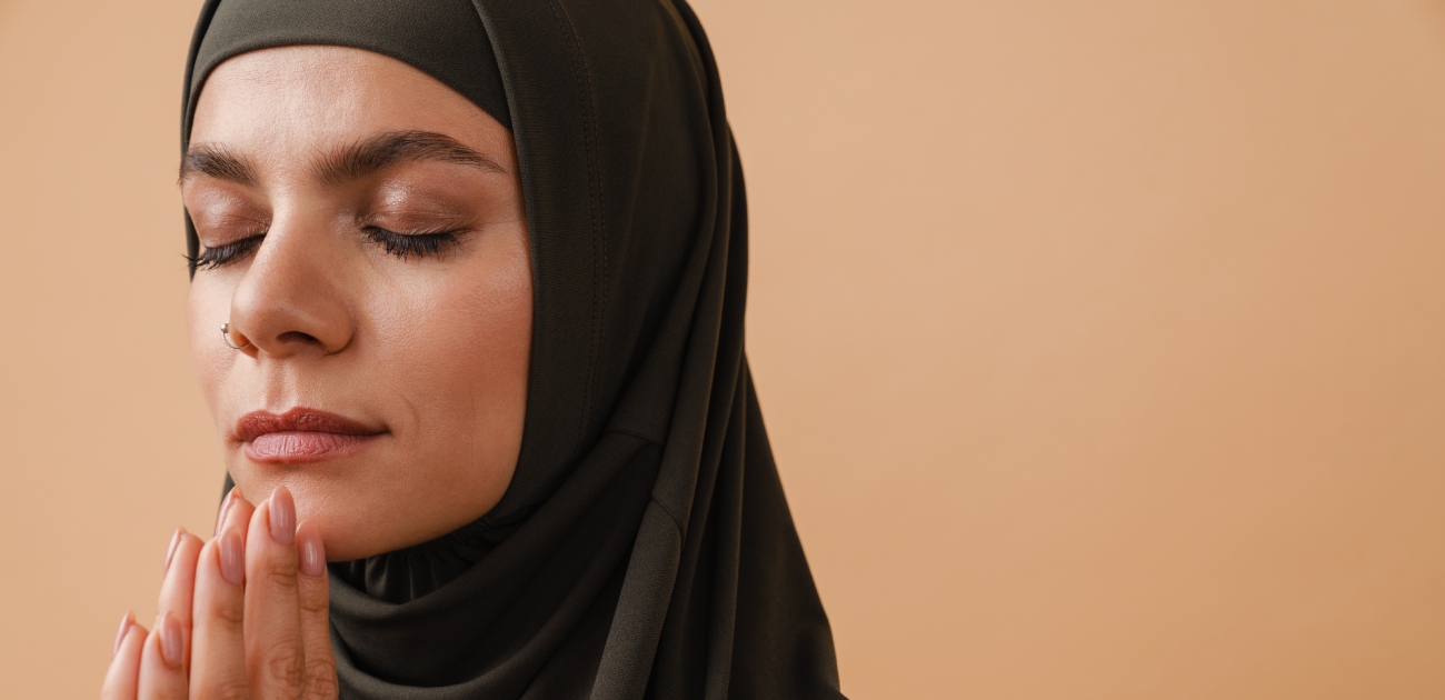امرأة مسلمة تغمض عينيها وتجمع يديها للدعاء